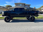 2007 Chevrolet Silverado 1500 black truck lifted 12 inches with aftermarket rims and tires parked on the street.