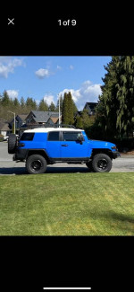 2007 Toyota FJ Cruiser in blue with off-road tires parked in front of houses.