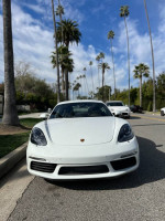 Front view of a white 2018 Porsche 718 Cayman parked on a palm-lined street