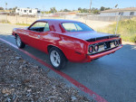 Red 1974 Plymouth Cuda parked on the street, showcasing its sleek design and chrome accents.