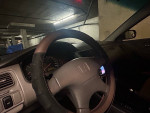 Interior view of a 1998 Honda Accord LX with leather steering wheel and dashboard in a parking structure.